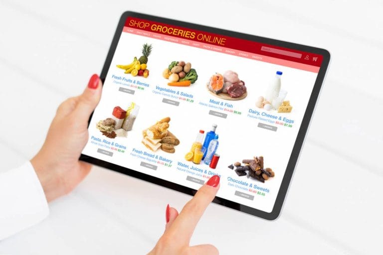 Personne utilisant une tablette pour acheter de la viande halal en ligne sur une boutique alimentaire avec différentes catégories de produits affichées à l’écran.
